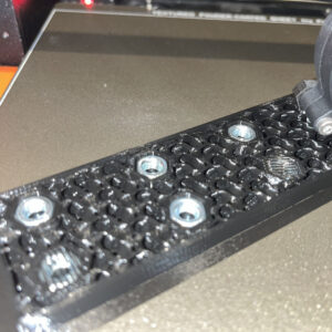 Galeria. Realizacja wydruku 3D. Wydruk cześci maszyny z zabudowanymi wewnętrz wydruku nakrętkami umożliwiającymi łatwy montaż śrubowy.